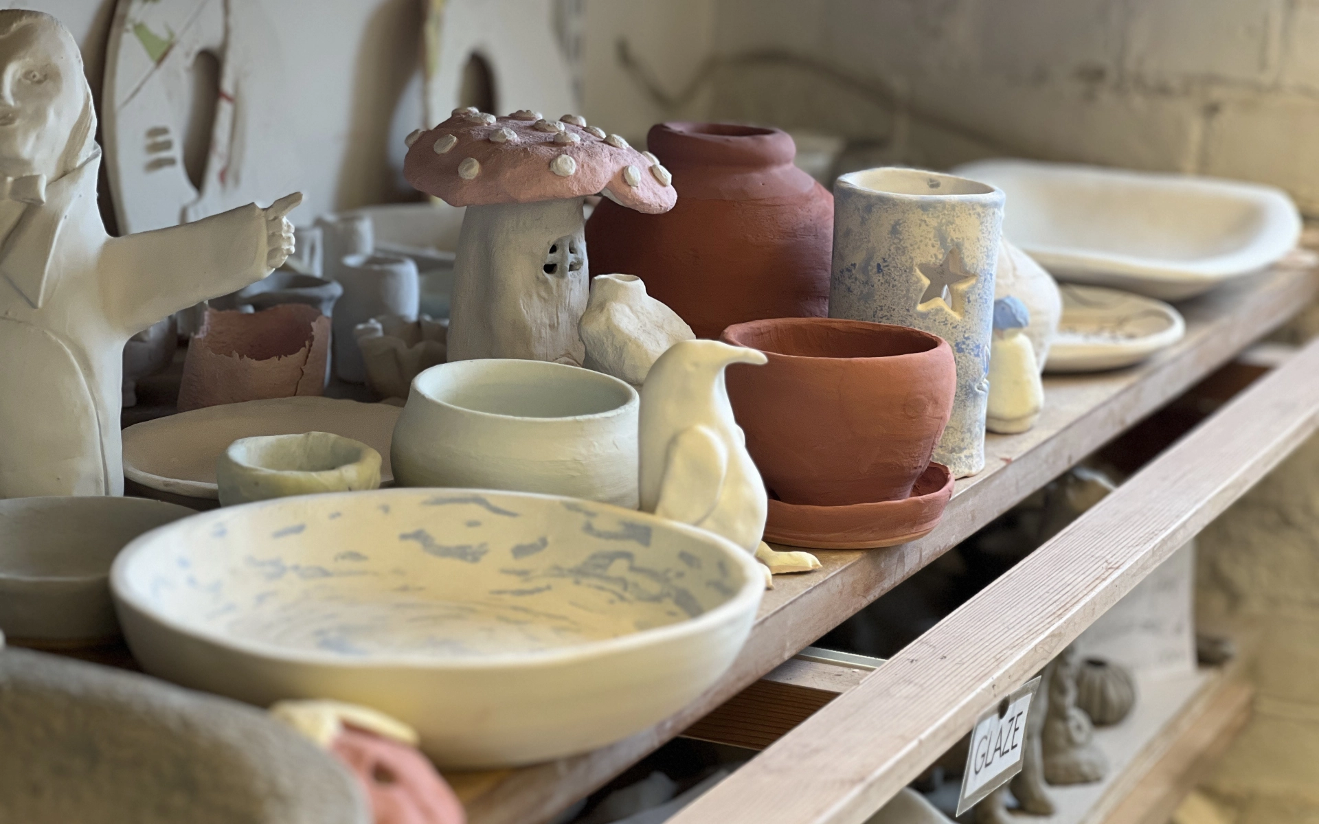 A shelf in a pottery studio, featuring several pottery works. Such as bowls, plates and sculptures.