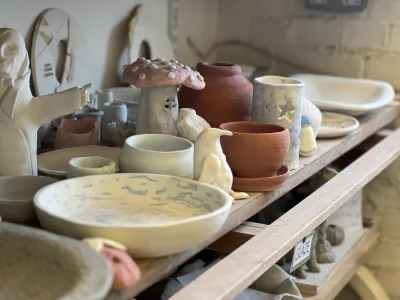 A shelf in a pottery studio, featuring several pottery works. Such as bowls, plates and sculptures.