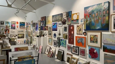 A bright art gallery with white walls and ceiling beams, densely packed framed paintings of landscapes, abstracts and portraits.