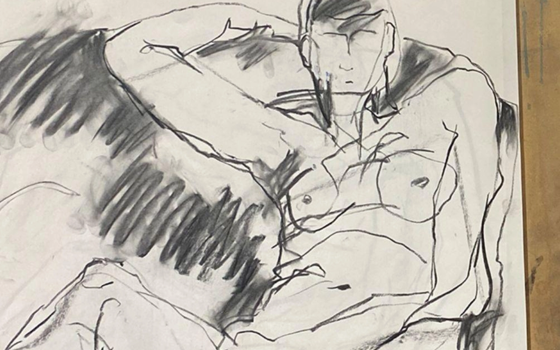 Charcoal drawing of a reclining nude figure on a surface, one arm behind the head; bold lines with heavy shading across the torso.