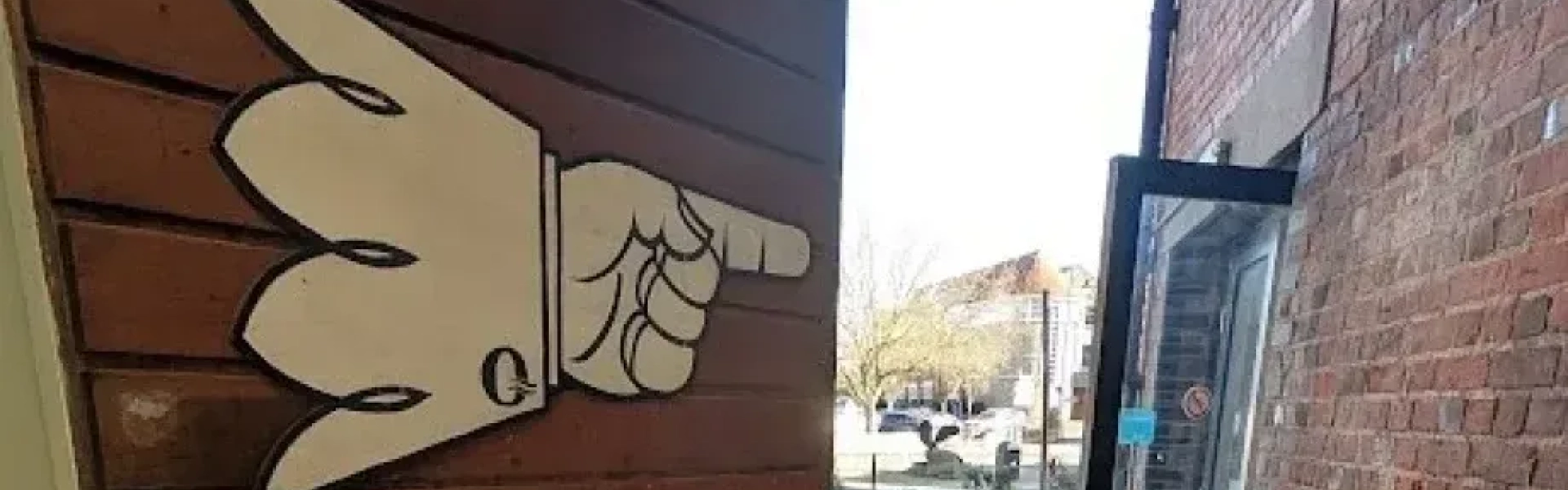 A large beige cartoon hand on a wooden wall points toward an open doorway leading to an outdoor patio with tables and chairs.
