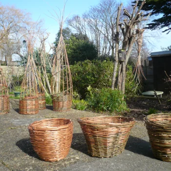 An image of three woven willow baskets in a garden space, giving an example of how your baskets will look upon completing the workshop.