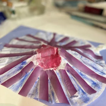 An image of a circular sea shell made from paper and tissue paper, painted with purple and blue watercolours.