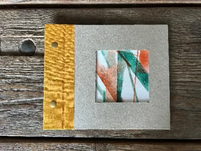 An imagine featuring a handmade sketchbook using scraps, unfinished prints and spare bits. It is squared, hand-bound and textured with a yellow spine.