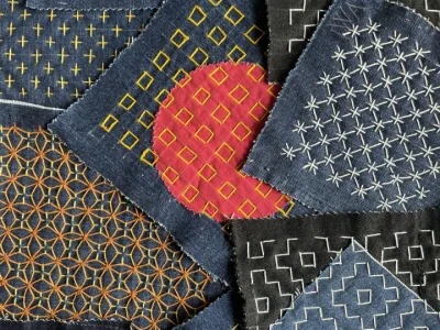 An image showing examples of square teal and dark green pieces of cloth, decorated with Sashiko Stitch pattern technique.