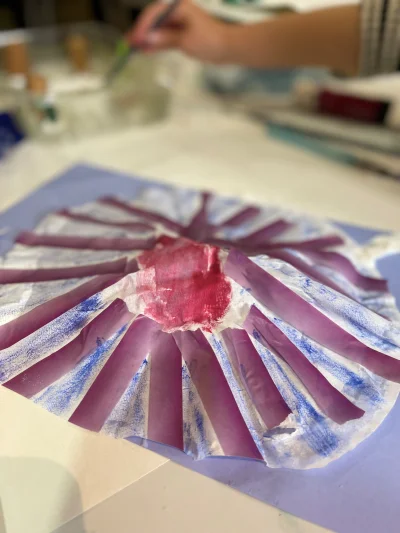 An image of a circular sea shell made from paper and tissue paper, painted with purple and blue watercolours.