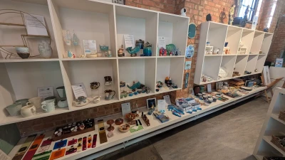 Bright brick-walled shop with white cubby shelves showcasing handmade pottery, glass figurines, and small crafts along a long display counter.