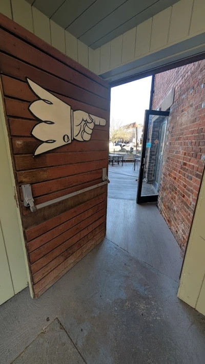 Open doorway to an outdoor seating area; a large white cartoon hand pointing to the right is mounted on a wooden wall beside a brick exterior.
